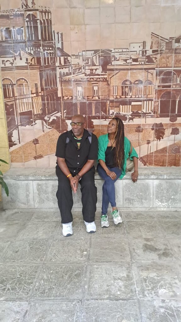 Joan and Hughie sit beside mural in Havana