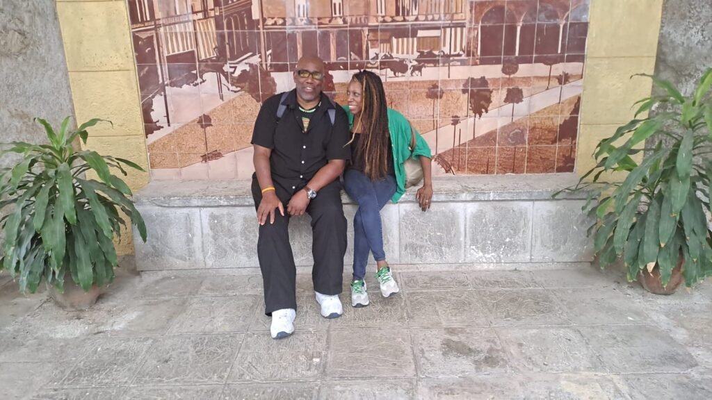 Joan and Hughie are amused whilst sitting beside mural in Havana