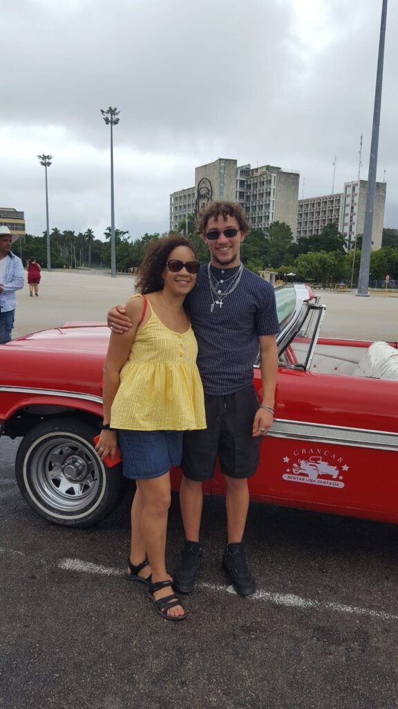 Travellers Jenni & Ty pose beside their red Cuban classic convertible car at Revolution Square