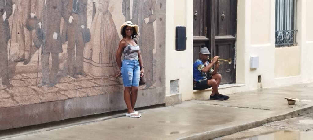 Brenda with musician posing by mural in Havana