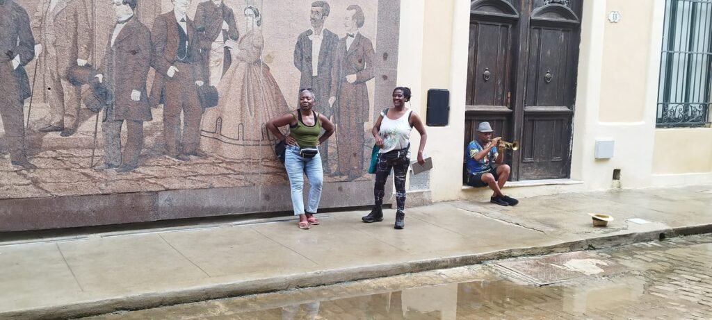 Kadija, Obi and musician chill by a mural in Havana